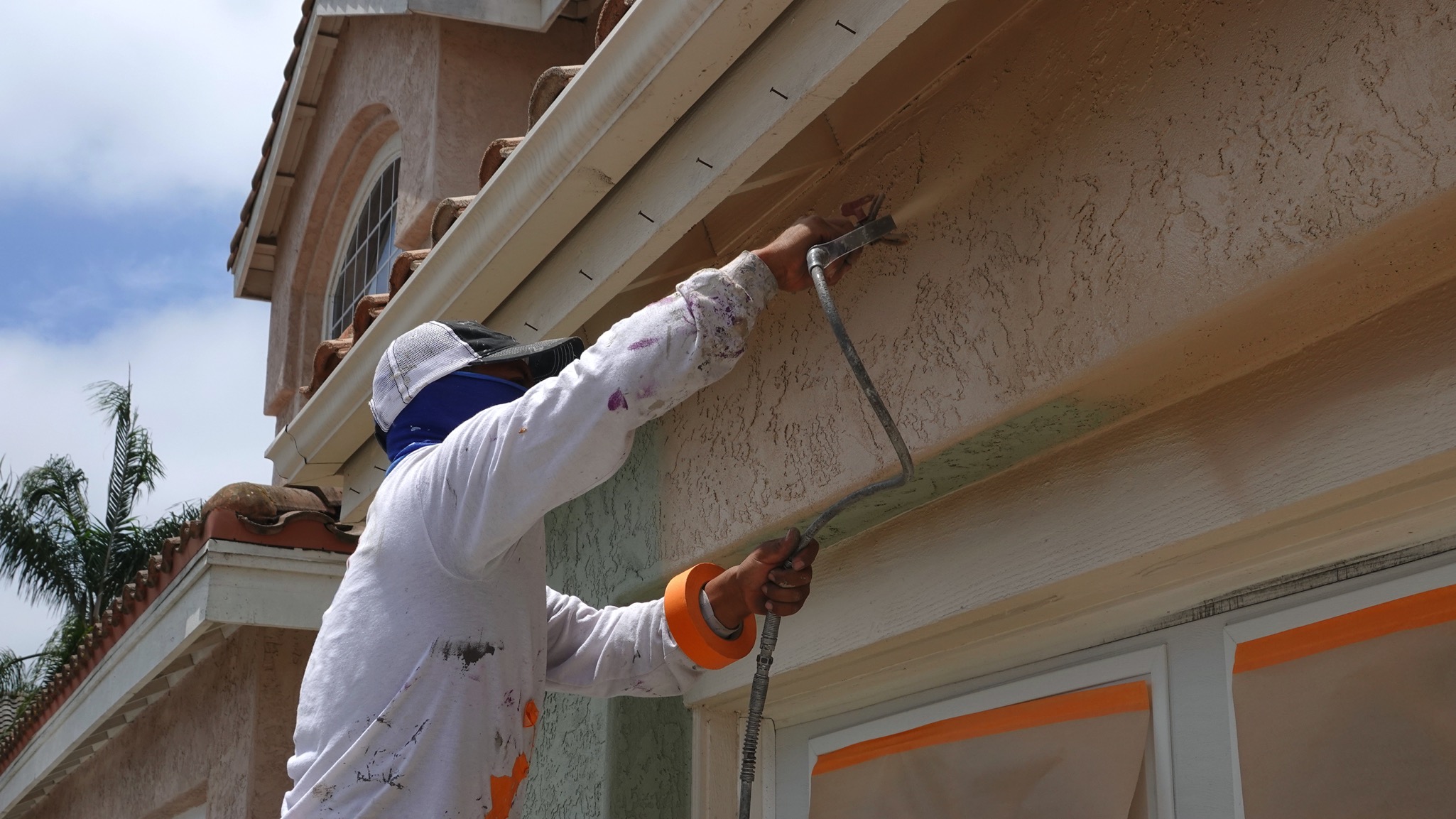 Professional painter using high-pressure spray gun for exterior house painting.